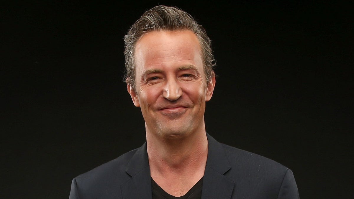 Matthew Perry posing in a black suit at a press call