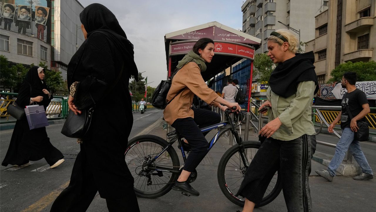 A woman rides a bicycle as others cross a street in downtown Tehran, Iran, Sunday, May 24, 2026. (AP Photo/Vahid Salemi)