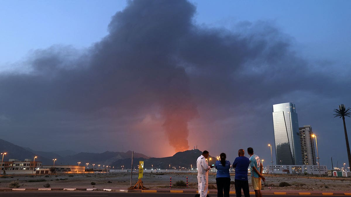 Foreign workers looking at tall plume of black smoke in Fujairah industrial zone