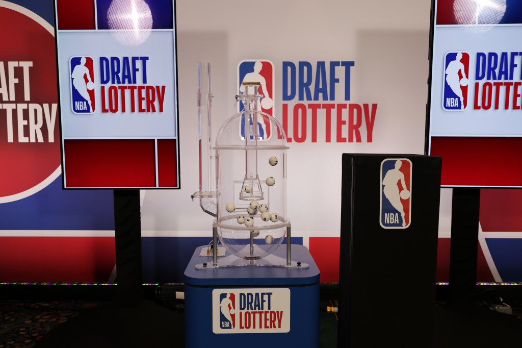 NBA Draft Lottery machine with numbered balls inside, flanked by screens displaying the NBA Draft Lottery logo.