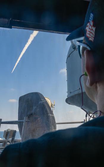 A sailor watches a missile fire from the deck of a ship.