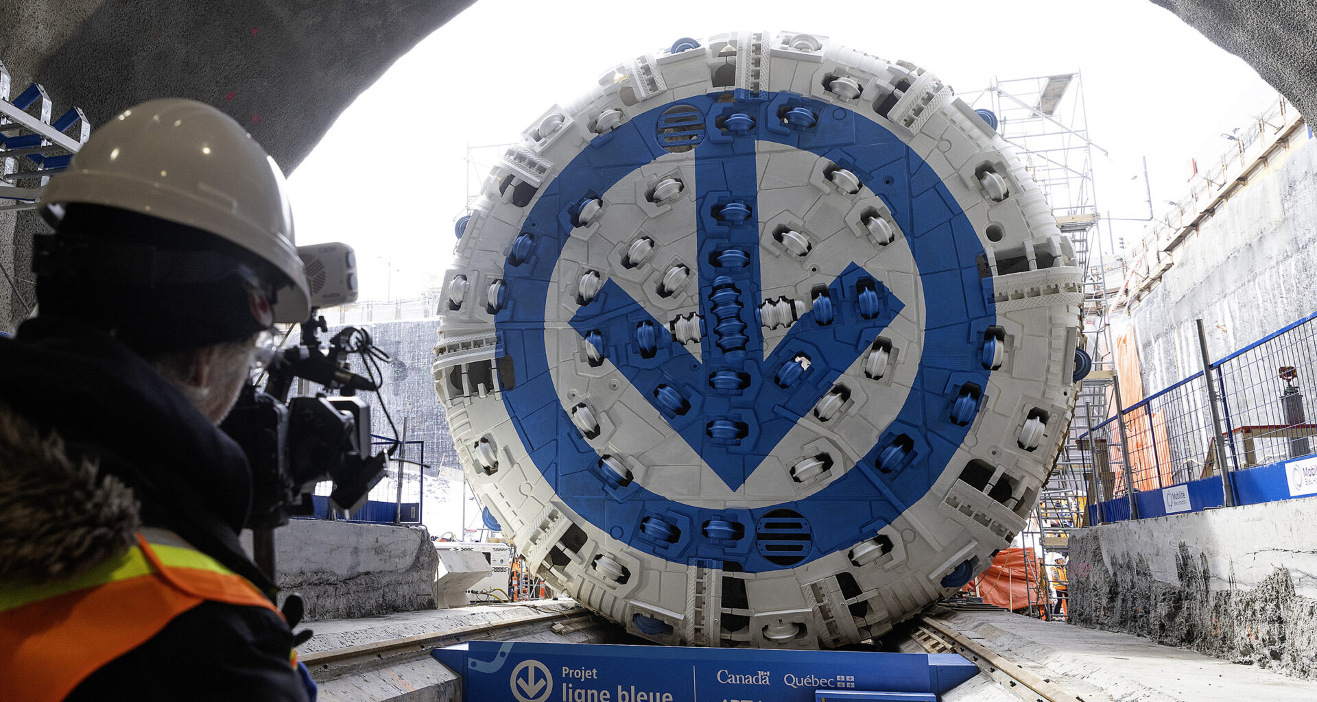 A tunnel borer with a blue and white métro logo painted on its cutting surface is seen at the entrance to a tunnel from inside the tunnel.