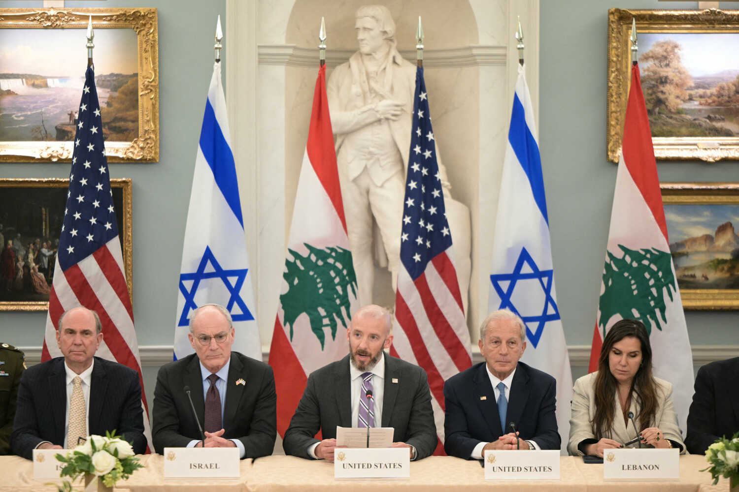 Four men and a woman sit at a table with microphones on it. The flags of the United States, Israel and Lebanon are displayed behind them.