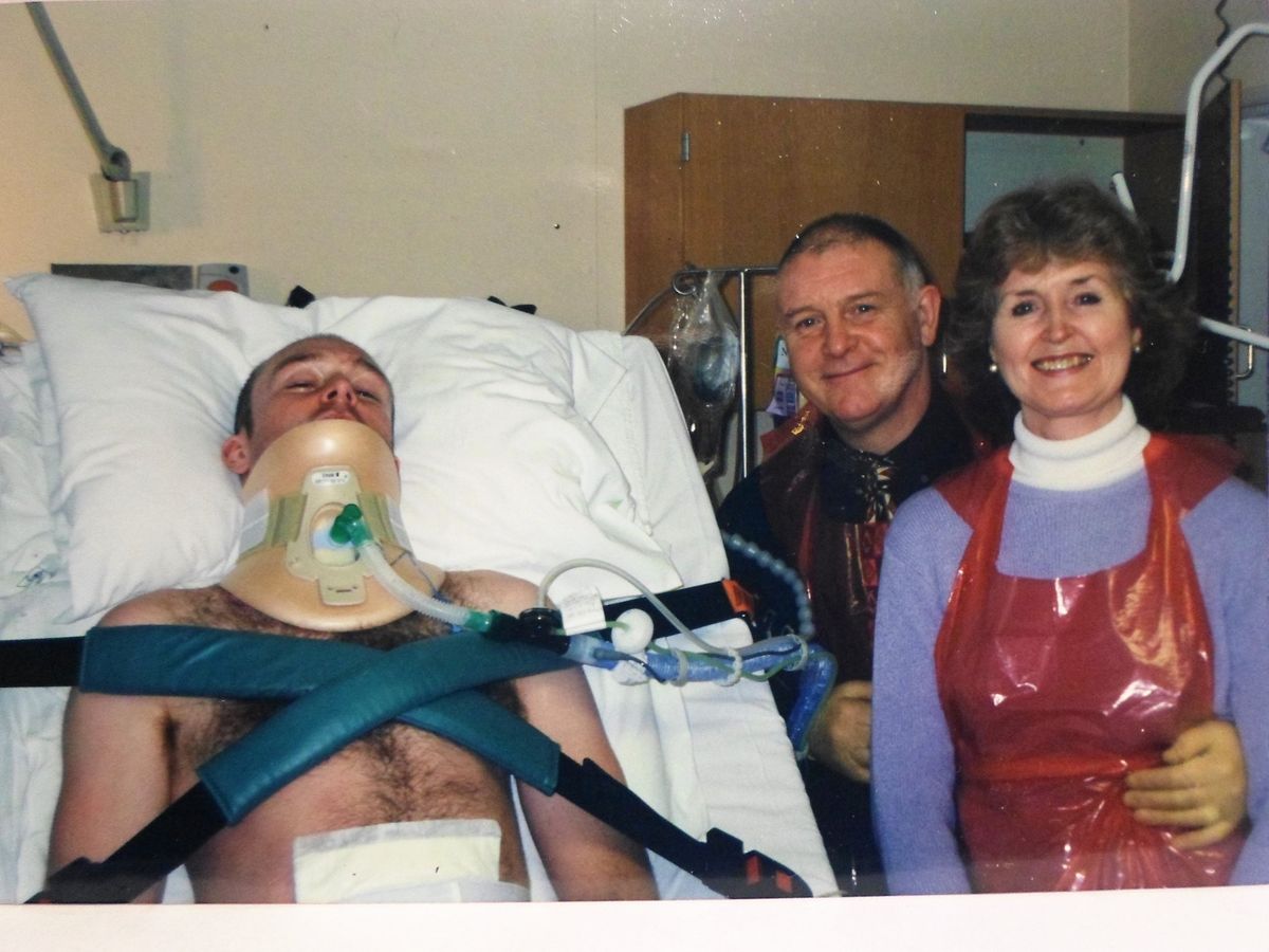 A badfly-injured man in a hospital bed with his parents by his side