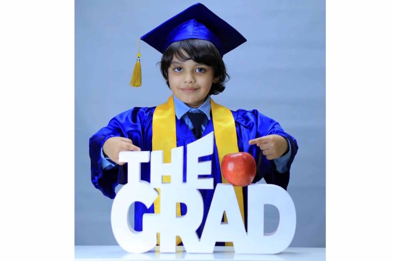 A photo of a school child in graduation gown with a sign that says "the grad"