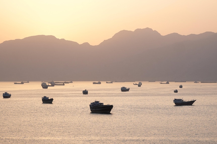 Ships sailing in the Strait of Hormuz with a setting sun behind them.