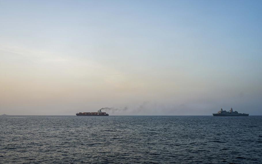 A container ship and a U.S. Navy warship sail in parallel in the Arabian Sea.