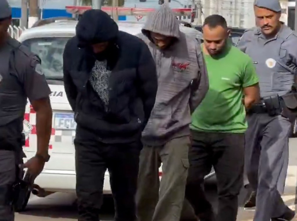 Three men in handcuffs are escorted by police officers.
