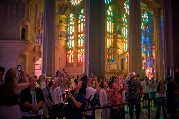 Visitors take photos inside Antoni Gaudí's Basilica of the Sagrada Familia as colored light from its stained-glass windows illuminates the interior in Barcelona, Spain, Tuesday, May 26, 2026, ahead of Pope Leo XIV's visit to the city in June. (AP Photo/Emilio Morenatti)