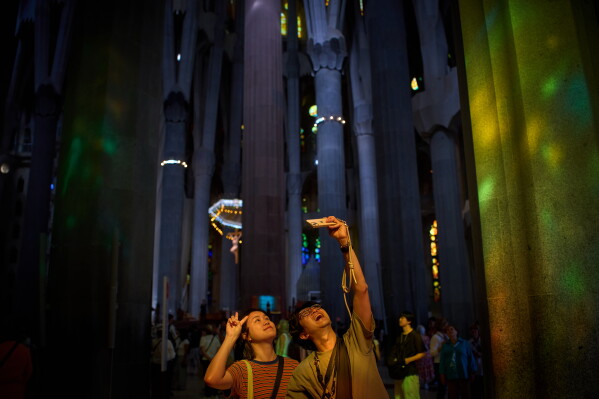 Visitors take photos inside Antoni Gaudí's Basilica of the Sagrada Familia as colored light from its stained-glass windows illuminates the interior in Barcelona, Spain, Tuesday, May 26, 2026, ahead of Pope Leo XIV's visit to the city in June. (AP Photo/Emilio Morenatti)