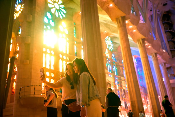 Visitors take photos inside Antoni Gaudí's Sagrada Família basilica as colored light from its stained-glass windows illuminates the interior in Barcelona, Spain, Wednesday, May 20, 2026, ahead of Pope Leo XIV's visit to the city in June. (AP Photo/Emilio Morenatti)