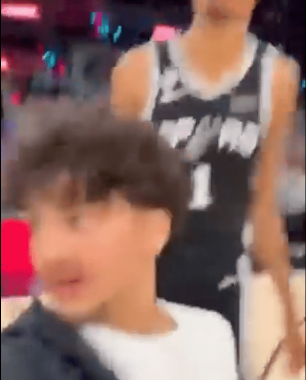 A young boy with curly hair in a white shirt and a blurred person in a number 1 sports jersey.