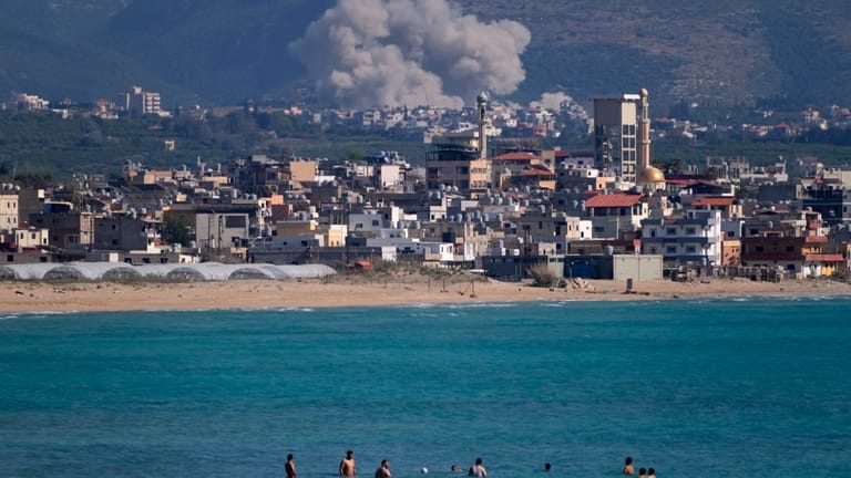 People swim on a public beach as smoke, background, rises...
