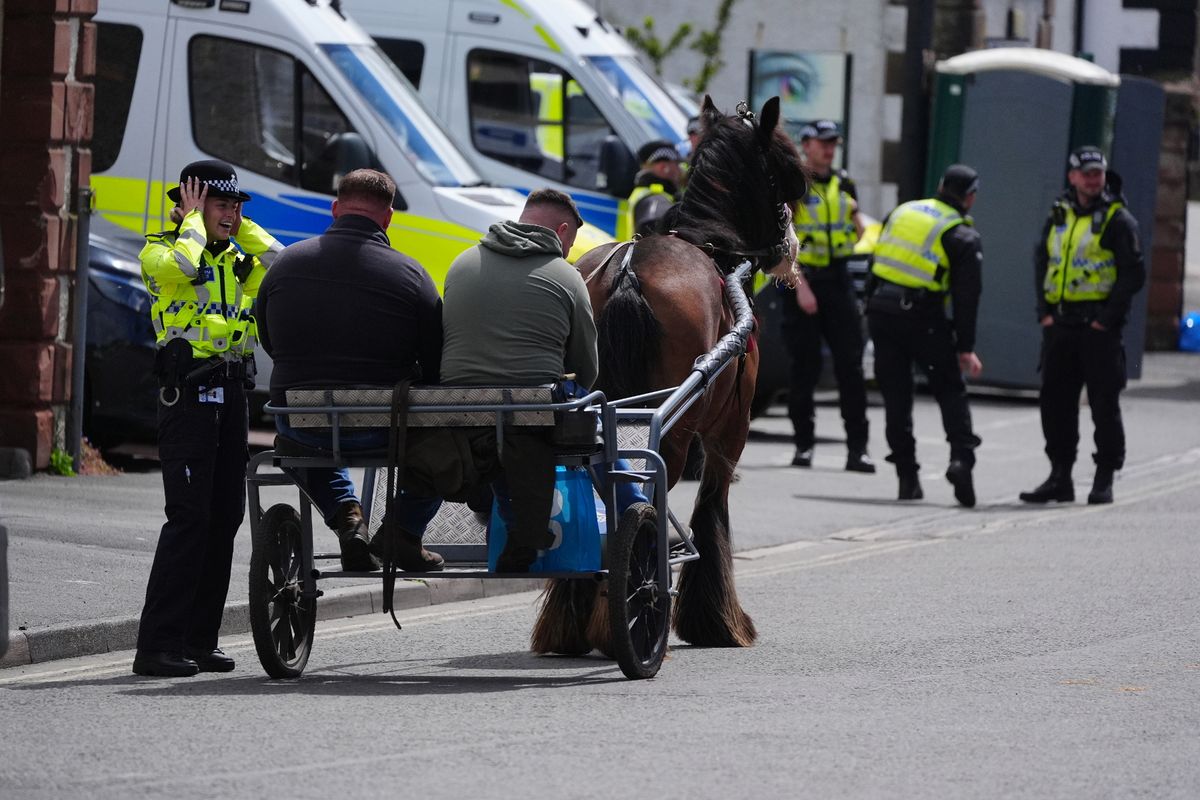 People in horse drawn carriages talk to a police officer during the Appleby Horse Fair