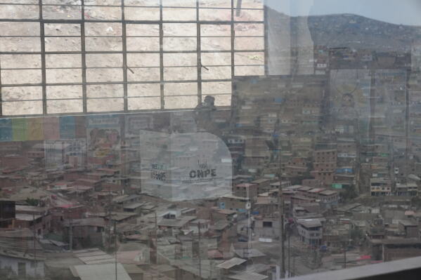 A voter, seen through a window reflecting San Juan de Miraflores district, marks a ballot during the presidential runoff election in Lima, Peru, Sunday, June 7, 2026. (AP Photo/Rodrigo Abd)