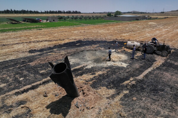 Farmers spray water in a burned agricultural field next to a projectile near the town of Najha, Syria, Monday, June 8, 2026, after debris from Iranian missile launches during the Iran-Israel conflict fell in the area. (AP Photo/Ghaith Alsayed)