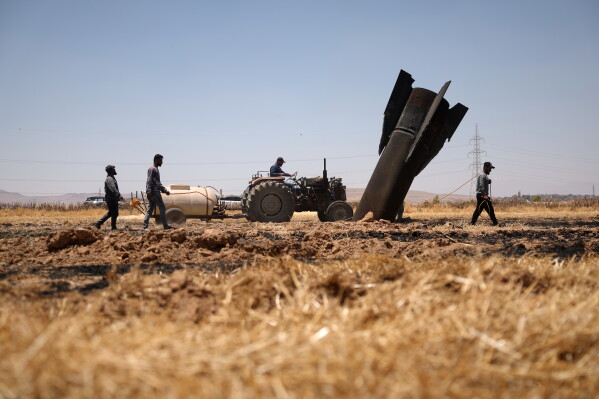 Farmers spray water in a burned agricultural field next to a projectile near the town of Najha, Syria, Monday, June 8, 2026, after debris from Iranian missile launches during the Iran-Israel conflict fell in the area. (AP Photo/Ghaith Alsayed)