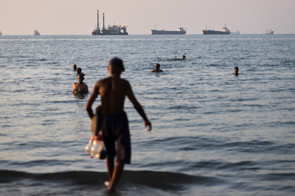 Resident swim as cargo and commercial vessels are anchored in the Strait of Hormuz off Bandar Abbas, Iran, Monday, June 8, 2026. (Amirhosein Khorgooi/ISNA via AP)