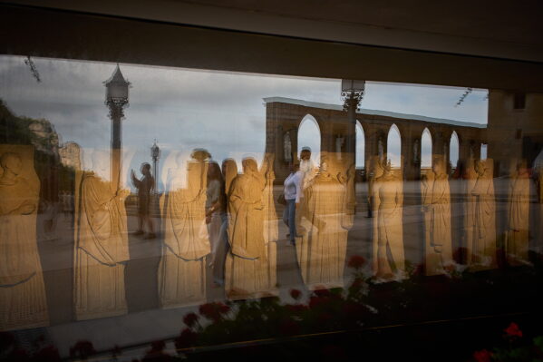 Tourists are reflected in the glass of a museum on the main square of the Monastery of Montserrat near Barcelona, Spain, Friday, June 5, 2026. (AP Photo/Emilio Morenatti)
