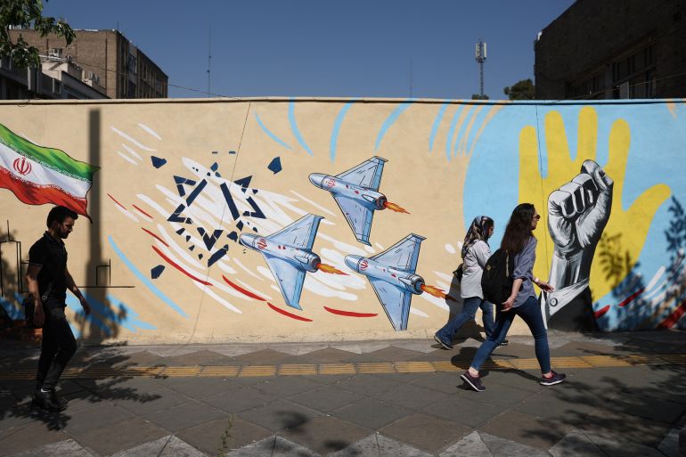 People walk next to an anti-Israeli mural on a street in Tehran,