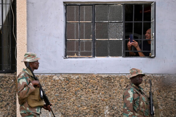 A resident uses a mobile phone to take a photograph of the South African National Defense Force officers deployed in the area, in the Riverlea township of Johannesburg, South Africa, March 11, 2026. (AP Photo/Themba Hadebe, File)