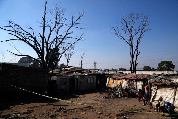 People sit outside a cordon, at the scene of a mass shooting at an informal settlement in the Cleveland suburb of Johannesburg, South Africa, Wednesday, June 10, 2026. (AP Photo/Themba Hadebe)