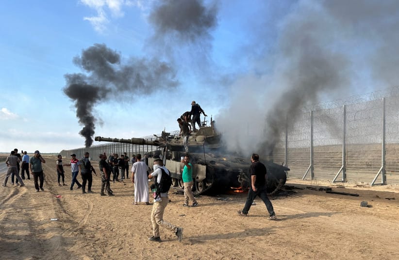 Palestinians react as an Israeli military vehicle burns after it was hit by Palestinian gunmen who infiltrated areas of southern Israel, at the Israeli side of Israel-Gaza border, October 7, 2023.