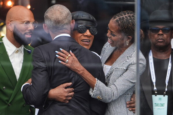 Former President Barack Obama, left, and former first lady Michelle Obama, right, embrace Stevie Wonder during the dedication ceremony for the Obama Presidential Center, Thursday, June 18, 2026, in Chicago. (AP Photo/Jeff Roberson)