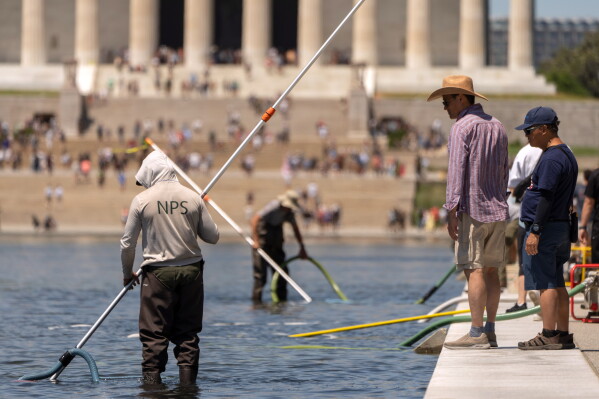 Visitors watch as National Park Service employees use vacuums to clean the Lincoln Memorial Reflecting Pool, Saturday, June 20, 2026, in Washington. (AP Photo/Mark Schiefelbein)
