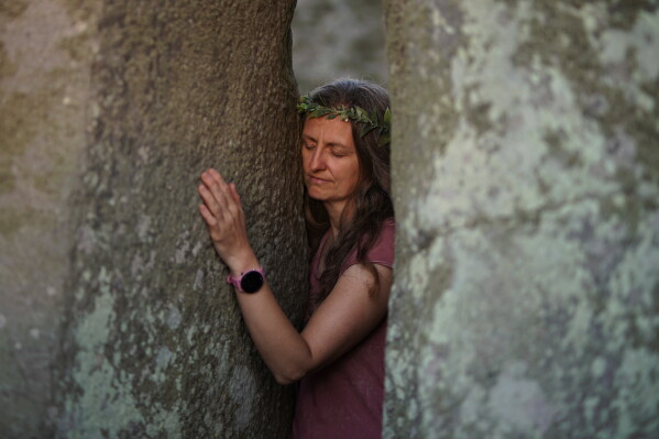 A reveler touches a stone at the ancient stone circle Stonehenge to celebrate the summer solstice, the longest day of the year, near Salisbury, England, on Saturday, June 20, 2026. (AP Photo/Alberto Pezzali)
