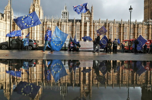 Protestors are reflected in a large puddle as they wave European flags to demonstrate against Brexit in front of the Parliament in London, Dec. 3, 2018. (AP Photo/Frank Augstein, File)