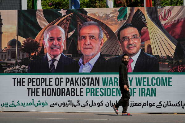 A man walks past a welcoming billboard featuring Iranian President Masoud Pezeshkian, center, with Pakistan President Asif Ali Zardari, right, and Shehbaz Sharif along a roadside in Islamabad, Pakistan, Tuesday, June 23, 2026. (AP Photo/Anjum Naveed)