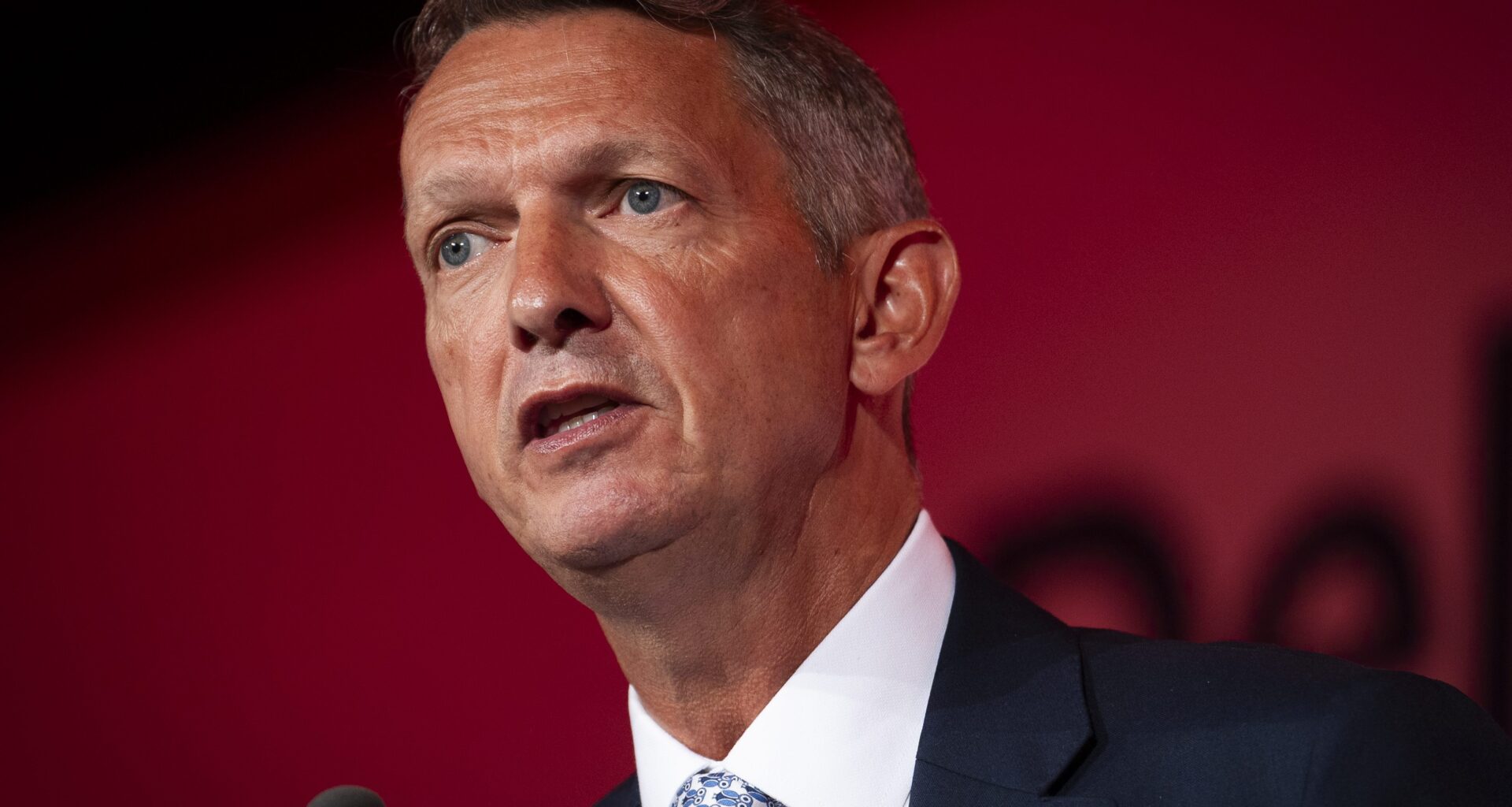 Andy Haldane speaking at a business conference, gesturing with hands, wearing a suit and tie, addressing economic issues.