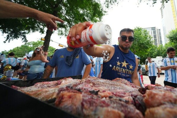 Lucas Martinez, of Dallas, an Argentina supporter, seasons meat with salt while grilling during a rally ahead of their team's World Cup Group J soccer match against Austria, Sunday, June 21, 2026, in Dallas. (AP Photo/Julio Cortez)