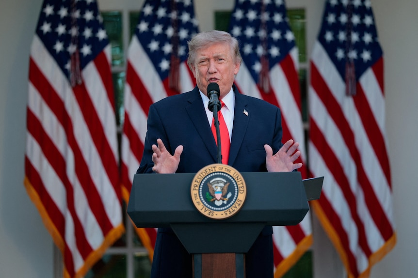 Donald Trump stands at a podium with US flags in the background. 