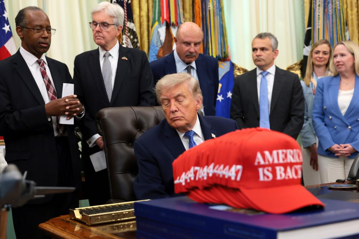 President Donald Trump closes his eyes as Dr. Ben Carson, left, speaks during an event in the Oval Office.