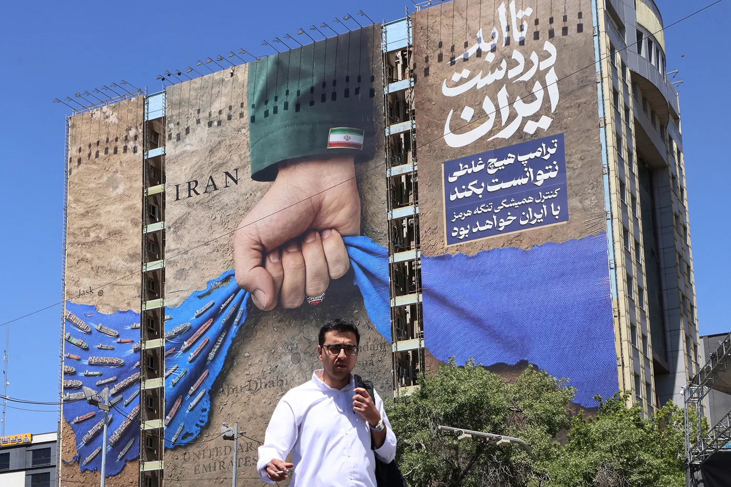 A man crosses a street past a billboard depicting the Strait of Hormuz with a caption in Persian reading “Forever in Iran’s Hand” at Vanak Square in Tehran.