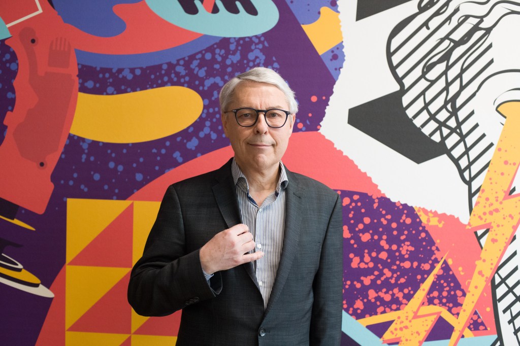 Claude Guillemot, co-founder of Ubisoft SA and CEO of Guillemot Corp., posing in front of a colorful, abstract wall art.