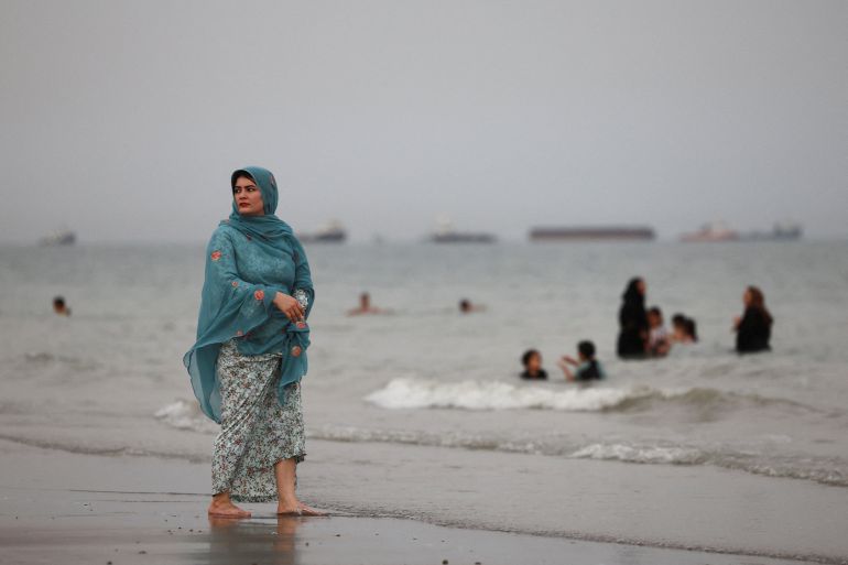 An Iranian woman walks on the beach as vessels in the Strait of Hormuz are visible near the beach of Bandar Abbas, Iran,