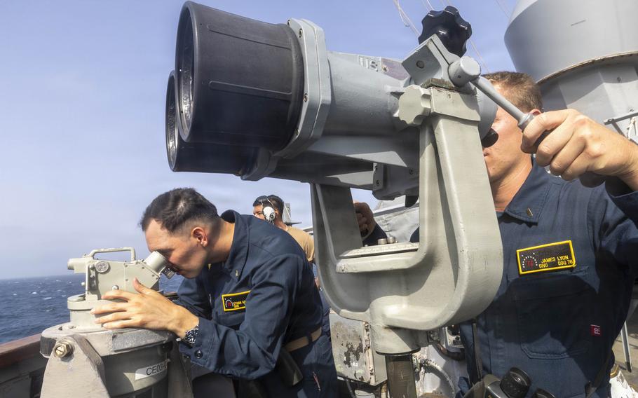 Sailors look through their shipboard-mounted binoculars.