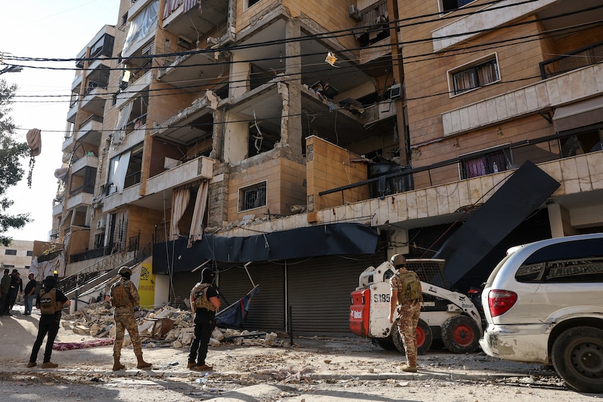 A group of men in military uniforms standing near a damaged building