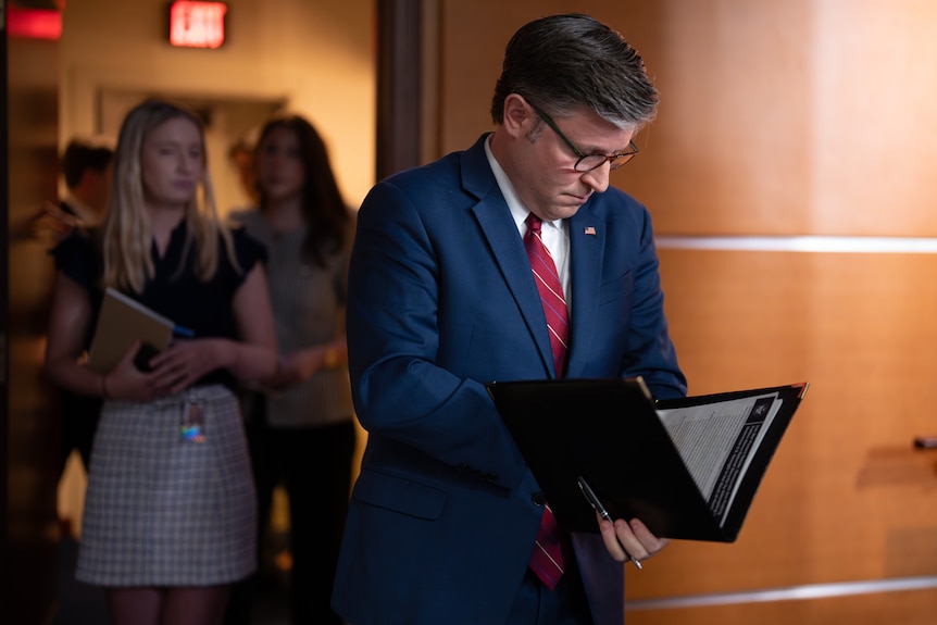 Mike Johnson reads from a binder as he walks through a hall.