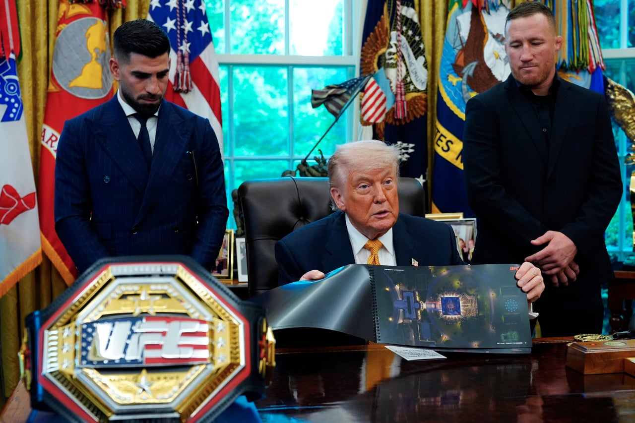President Donald Trump holds up an image depicting a preview of the "big fight" happening on the South Lawn on June 14, as UFC fighters Ilia Topuria, left, and Justin Gaethje listen, during a meeting on Wednesday, May 6, 2026, in the Oval Office of the White House, in Washington.