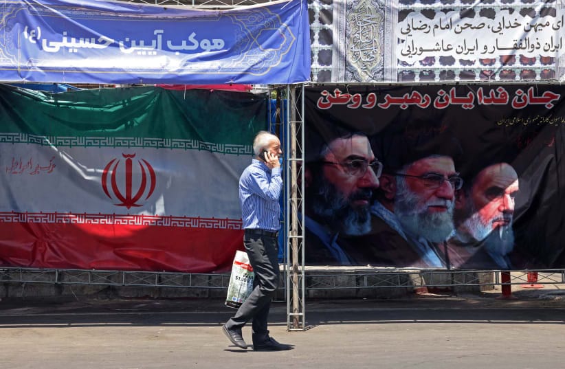 A man walks past Iran’s national flag and a banner bearing the images of the late founder of the Islamic Revolution, supreme leader Ayatollah Ruhollah Khomeini (R), the late Iranian supreme leader Ali Khamenei and his son, the current supreme leader Mojtaba Khamenei (L), in Tehran, June 10.