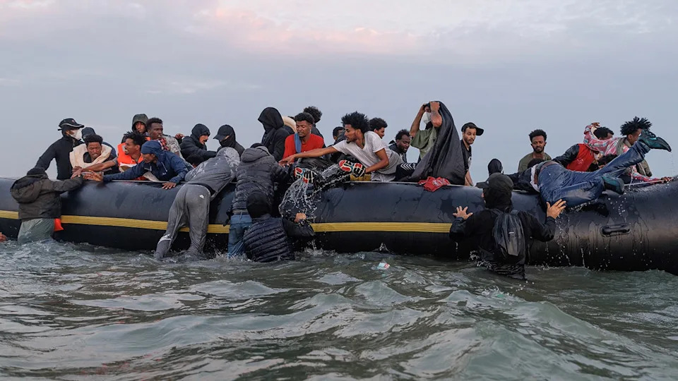 Migrants wading into water near Gravelines, France, with traffickers managing the scene