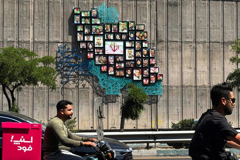 Men ride their mopeds past a map of Iran with the images of some of those killed in the Israeli-US war against the nation, erected on a wall along the highway in Tehran on June 17, 2026.