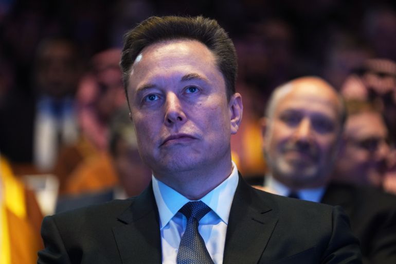 Elon Musk looks on.