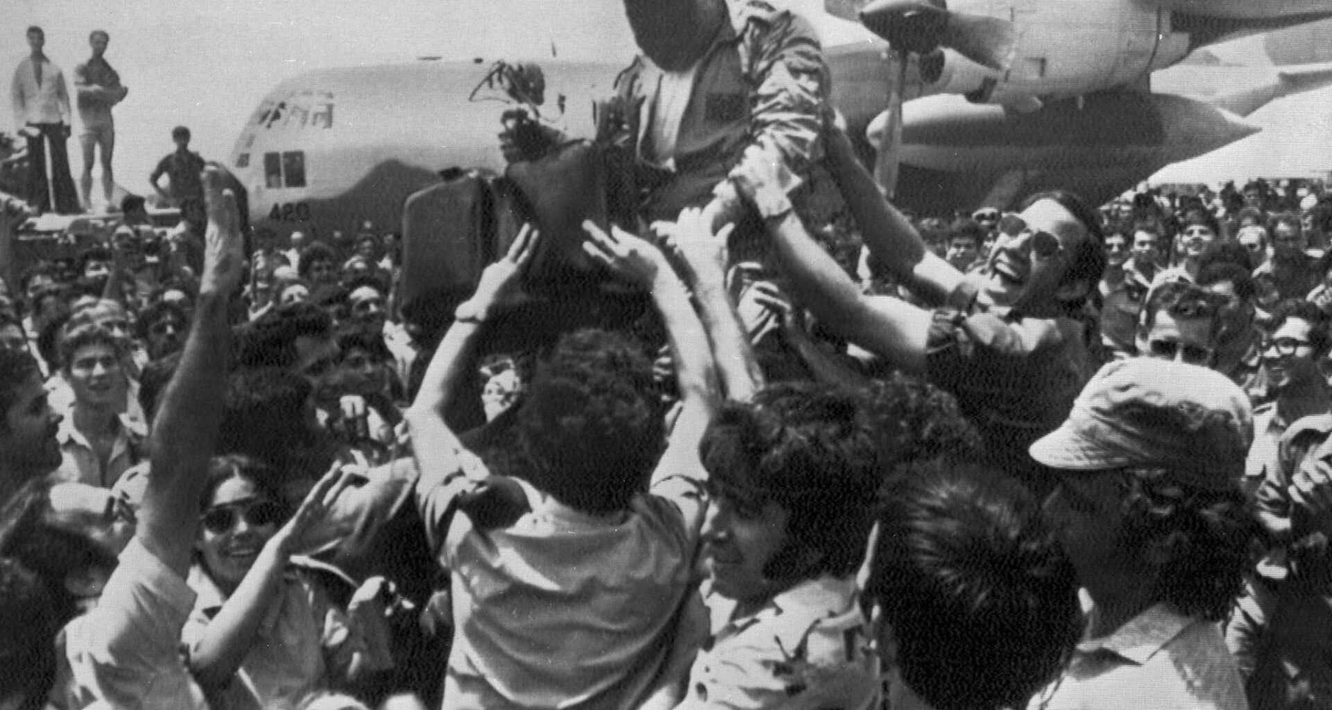 A cheering crowd at Ben-Gurion Airport raises a soldier in the rescue squad that freed the hijacked hostages from Uganda earlier in the day, July 4, 1976.  In the background is the C-130 transport plane which took part in the raid. The rescuer's face is obscured for security reasons. (AP Photo/Pool)