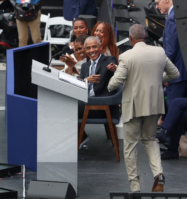 Former President Barack Obama, with former First Lady Michelle Obama and their daughters, laugh as family friend and Obama Foundation Chair Marty Nesbitt takes the stage wearing a tan suit during the Obama Presidential Center opening ceremony, June 18, 2026. Obama wore a tan suit during his presidency, causing controversy among conservative politicians. (John J. Kim/Chicago Tribune)