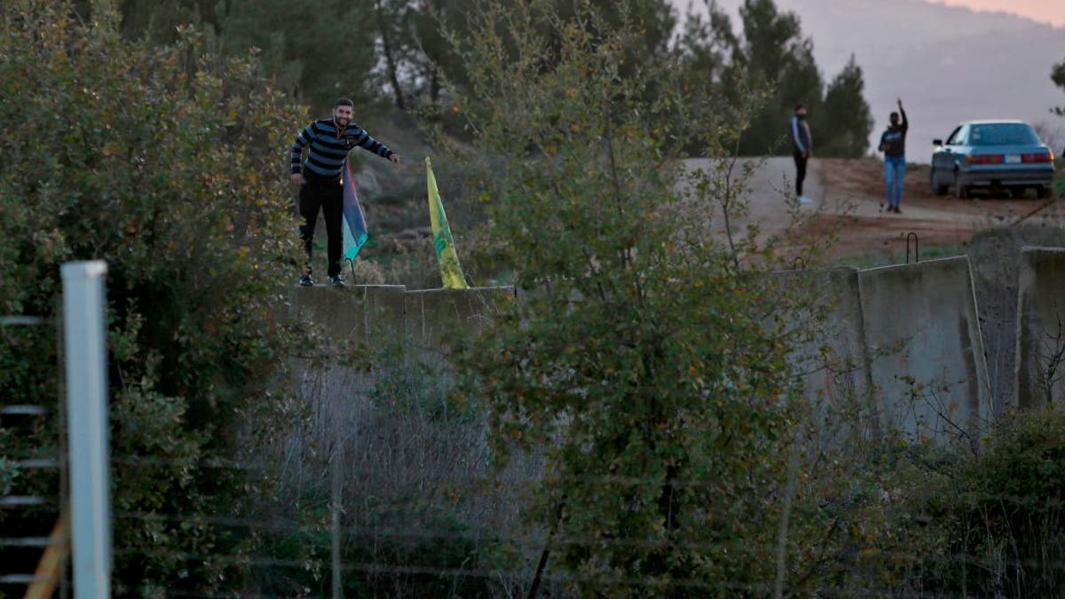 Lebanese man holding Hezbollah flag near border with Israel in southern Lebanese village of Hula